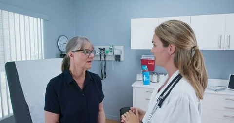 Female doctor talking to senior woman patient about neck problems in exam room Stock Footage