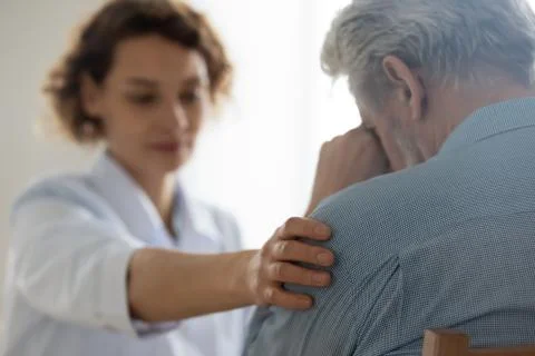 Female doctor touching shoulder comforting upset senior patient, closeup Stock Photos