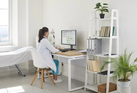 Female doctor using desktop computer in clinic office, managing patient records Stock Photos