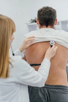 A female doctor in a white coat using a stethoscope to examine a male patie.. Stock Photos