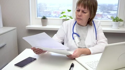 Female doctor working at a table with a computer and documents Stock Footage 304657912
