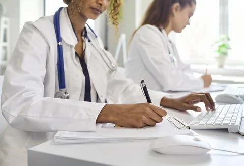 Female doctors writing notes and entering medical data at desktop computers Foto stock