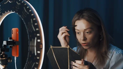 Female does her brows with brush holding mirror in hands in front of ring light Stock Footage 121607456