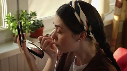 Female doing daily makeup routine while sitting by the window Stock Footage 336856522