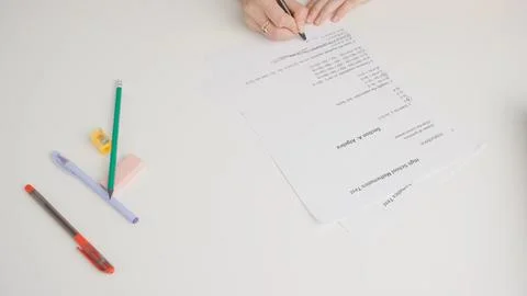 Female draws correct answer in math exam test paper with pencil. Student filling Stock Photos