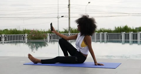 A female dressed for exercise sits on a yoga mat talking smart phone video call. Stock Footage 196146362