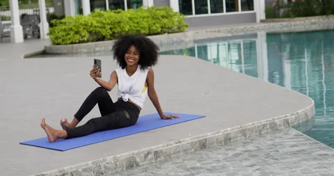 A female dressed for exercise sits on a yoga mat talking smart phone video call. Stock Footage 196146446