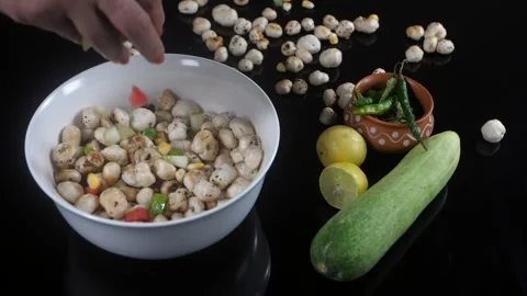 Female dropping slices of corn, tomato, and cucumber into a bowl of Makhana -... Stock Footage 161006424
