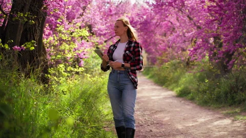 Female ecologist with digital tablet study flowering trees in park, walk al.. 動画素材 333580442
