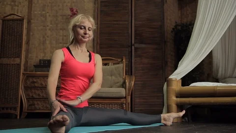 Female elderly blonde is sitting and stretching muscles at Buddha statue in room Stock Footage 87322945