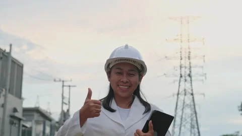 Female electrical engineer thumbs up and smiles on high voltage poles background Stock Footage 204970718