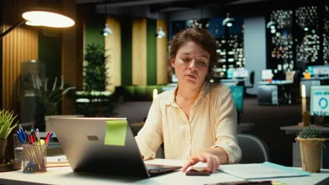 Female employee checking the time on her phone and closing laptop Stock Footage 317961854