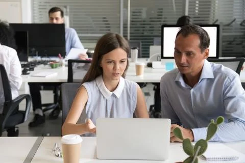 Female employee explaining computer task to male coworker workin Stock Photos