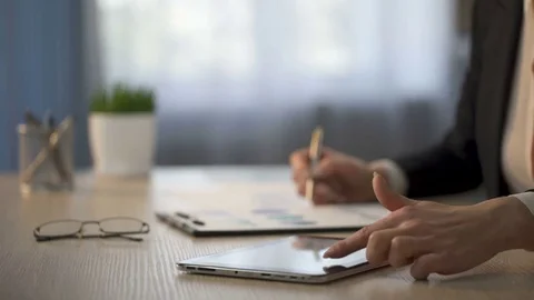 Female employee looking for information on tablet, marking printout graphs, data Stock Footage