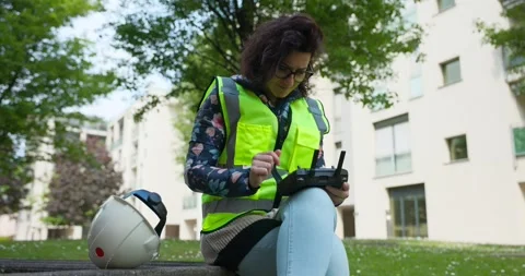 Female Engineer Checking Remote Controller For Aerial Drone Whilst Sat On Stock Footage 245793289