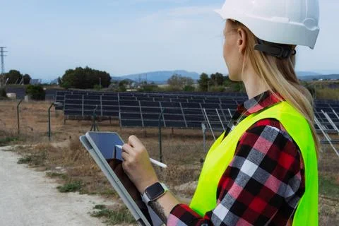 Female engineer in hard hat and safety vest checking solar panel performanc.. Stock Photos