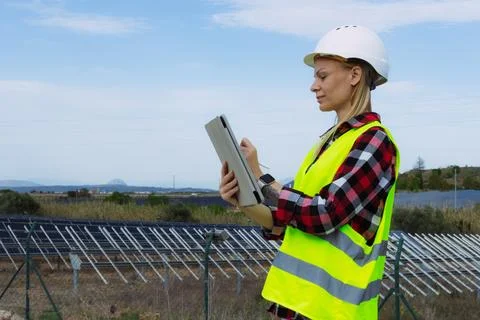 Female engineer in hard hat and safety vest reviewing data on a digital tab.. Stock Photos