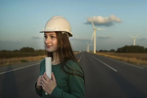 Female engineer in hard hat with plans by road at wind farm, looking left vie Stock Photos