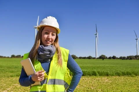 Female engineer holding tablet and inspecting wind turbines in green field Stock Photos