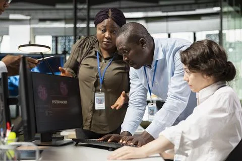 Female engineer in office requests help from coworkers to block hacker intrusion Foto stock