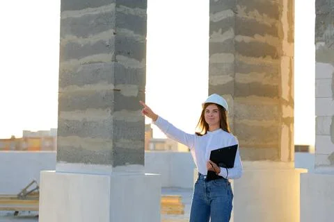 Female engineer pointing at construction site while holding clipboard Stock Photos