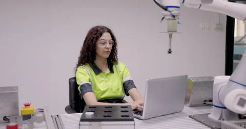 Female engineer with safety glasses programs automation system using laptop Stock Footage 313649262
