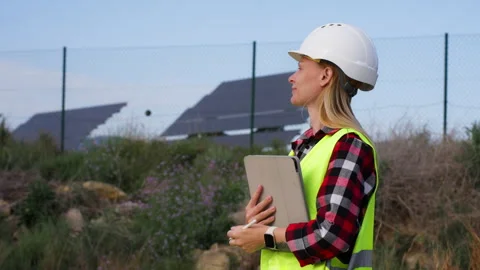 Female engineer in safety vest using tablet for inspecting solar panel farm.. Stock Footage 333581582