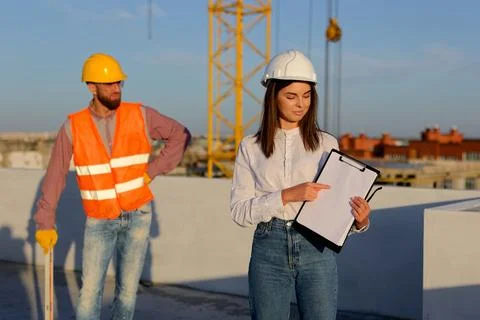 Female engineer showing a document to a construction worker on a rooftop Stockfoto's