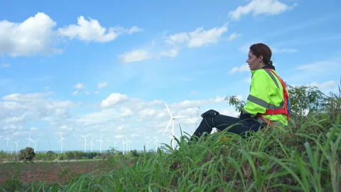 Female engineer sitting relax on the grass with wind turbines Stock Footage 253986892
