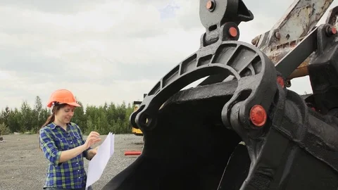 Female engineer standing next to a ladle of a excavator and examines a scheme Stock Footage 80207365