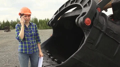 Female engineer standing next to a ladle of a excavator and examines a scheme Stock Footage 80865199