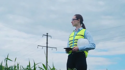 A female engineer stops on the road in front of a high voltage power line, takes 스톡 동영상 241801740