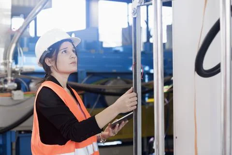 Female engineer using a digital tablet and examining the machine in an industria Stock Photos