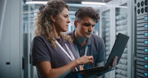 Female Engineer Using Laptop While Teammate Inspects Server Rack Stock Footage 344880120
