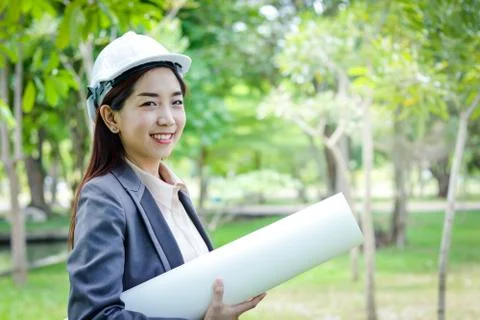 Female engineer wearing a white safety helmet holding a paper roll Stock Photos