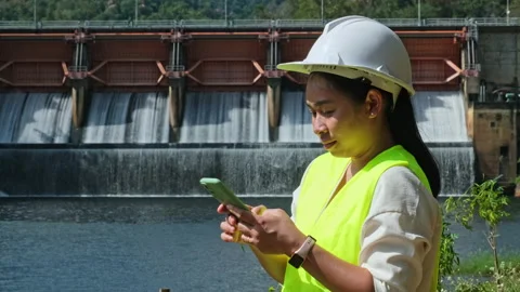 Female engineer working with smartphone and looking away at dam Stock Footage 229709268