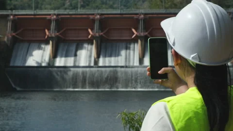 Female engineer working with smartphone and looking away at dam Stock Footage 229709525