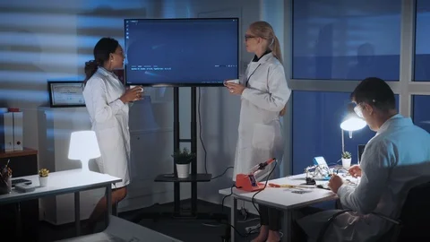 Female engineers talking about something near the TV screen with cup of drink Video stock 112876433