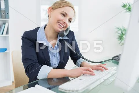 Female executive using landline phone and computer at desk Stock Photos