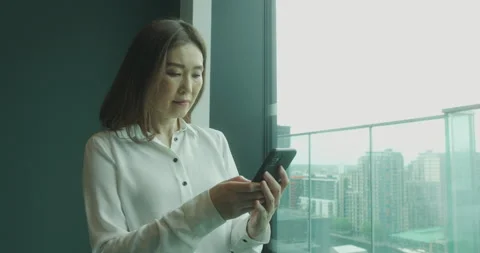Female Executive Using Smart Phone at Window Looking out on City Stock Footage 197028003