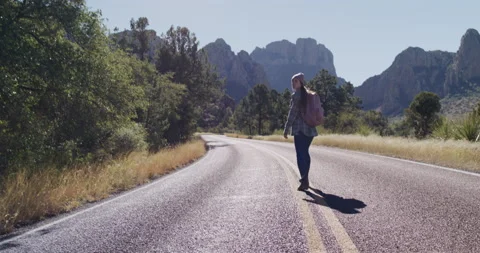 Female Explorer Walks Down Middle of Highway and Looks Back Stock Footage 238554888