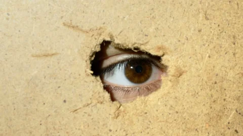Female eye looking through hole in wall Stock Footage 88664779