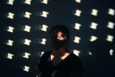 Female face emerging from dramatic light and shadow cast through a window. .. Stock Photos