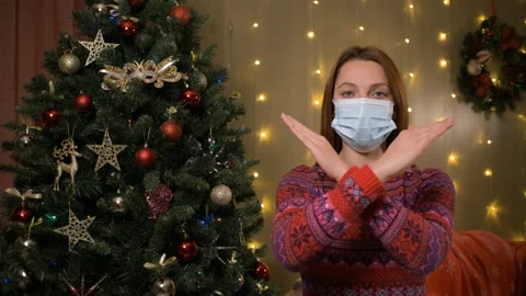 Female in face mask looks in camera standing next to decorated Christmas tree Stock Footage 165437207