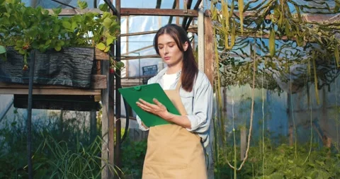 Female farmer makes notes with pen in folder. Gardener in apron looks at Video stock 244618183