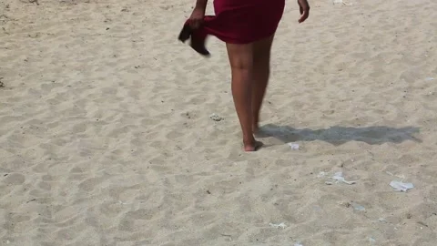Female feet on the sand in a developing red dress. An Stock Footage 157979053