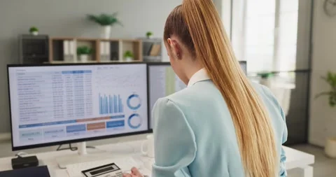 Female financial analyst reviewing data dashboards on computer screens at office Stock Footage 342430973