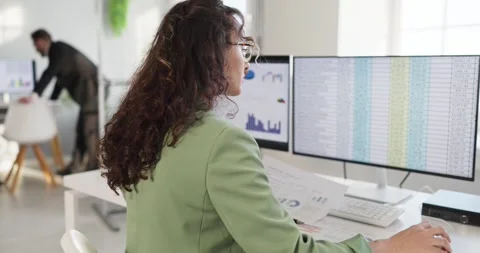 Female financial analyst working on spreadsheets at dual monitors in modern Stock Footage 329924842
