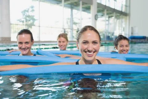 Female fitness class doing aqua aerobics with foam rollers Stock Photos