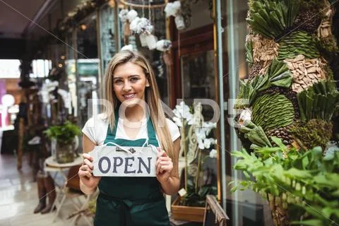 Female Florist Holding Open Signboard Outside The Flower Shop